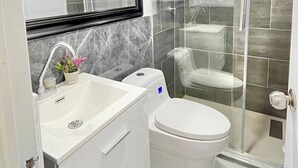 Un baño moderno con cabina de ducha de vidrio, un lavamanos blanco y una meseta de mármol, y un inodoro.