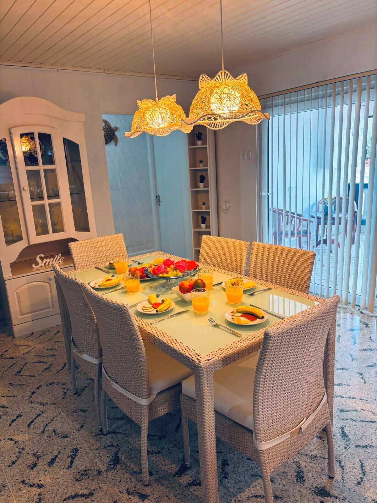 A dining area with wicker chairs, a glass-top table, and a fruit platter.