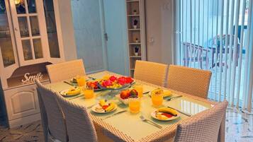 A dining area with wicker chairs, a glass-top table, and a fruit platter.