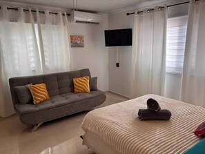 A bedroom with a grey sofa, a bed with a white textured bedspread, and a flat-screen TV on the wall. - Fabulous 3-bedroom house with AC in charming Savaneta (Savaneta)
