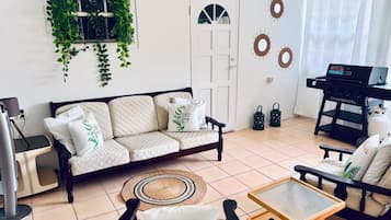 A living room with a sofa, a coffee table, a TV stand, a grill, and decorative wall art.
