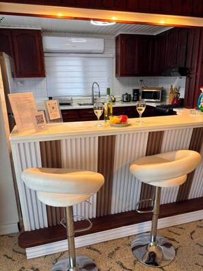 A kitchen with a bar area, two bar stools, a microwave, and a sink. - Fabulous 3-bedroom house with AC in charming Savaneta (Savaneta)