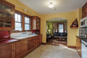 A kitchen with wooden cabinets, a large sink, and a dining area with a sofa and rug. - Spacious 4-bedroom house in fabulous Sparrow Bush with AC (Sparrow Bush)