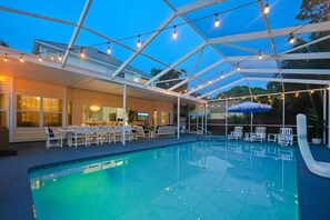 A swimming pool with lounge chairs and umbrellas, surrounded by a covered patio area with string lights. - Heated Pool + Spa, Game Room, 5BR/4BA, 5 Min to Indian Shores Beach (Seminole)