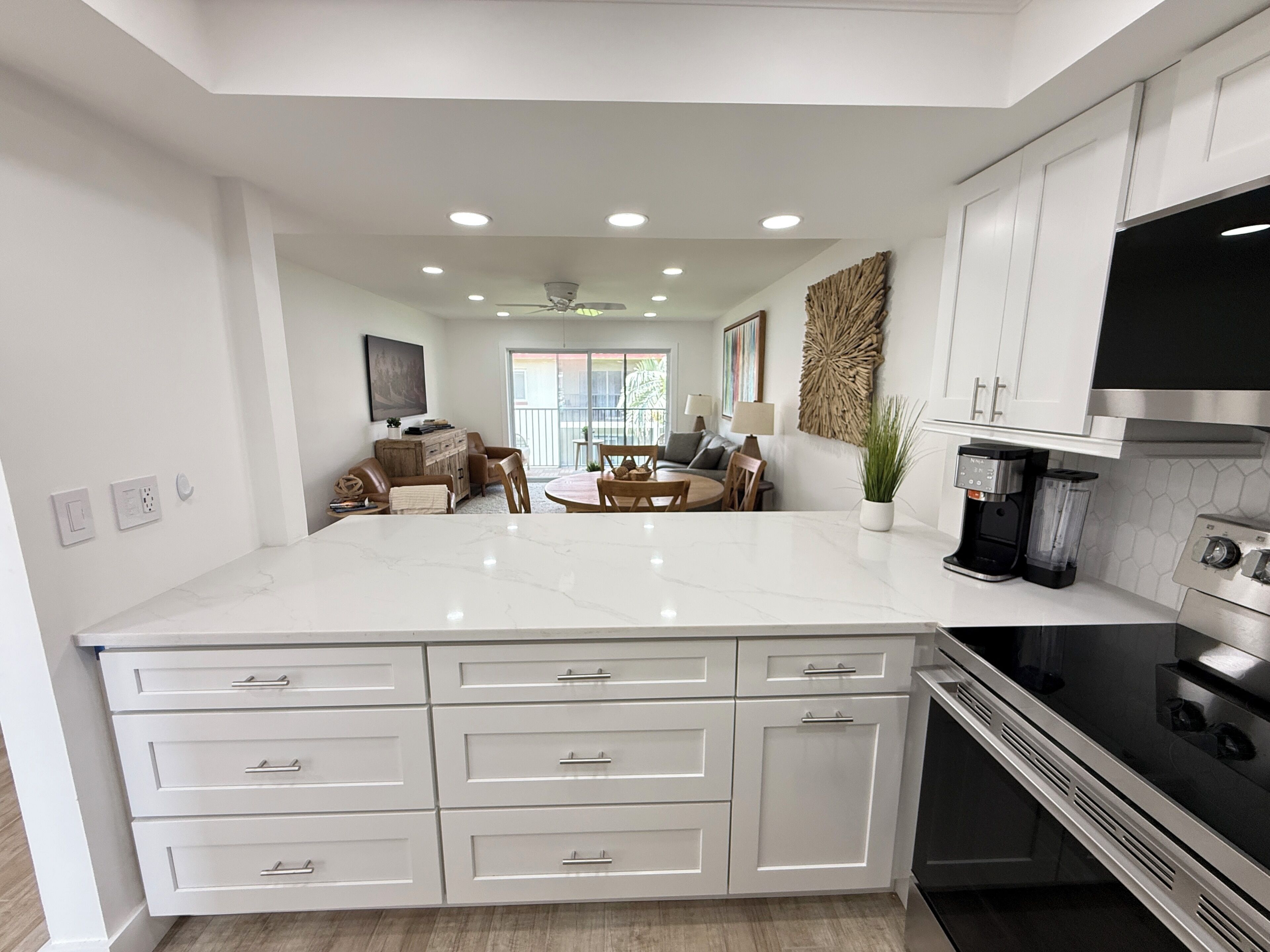 A modern kitchen with white cabinetry, a marble countertop, and a dining area with a table and chairs.
