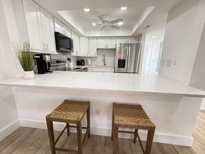 A modern kitchen with white cabinetry, a large island, stainless steel appliances, and a ceiling fan. - Cozy 2-bedroom condo in lovely St. Augustine across from the beach and Fun (St. Augustine)