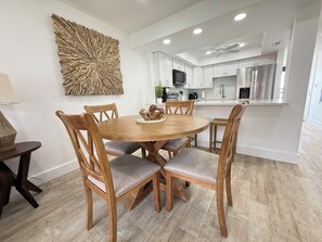 A modern kitchen with white cabinets, a central island, and a dining area with wooden chairs and a round table. - Cozy 2-bedroom condo in lovely St. Augustine across from the beach and Fun (St. Augustine)
