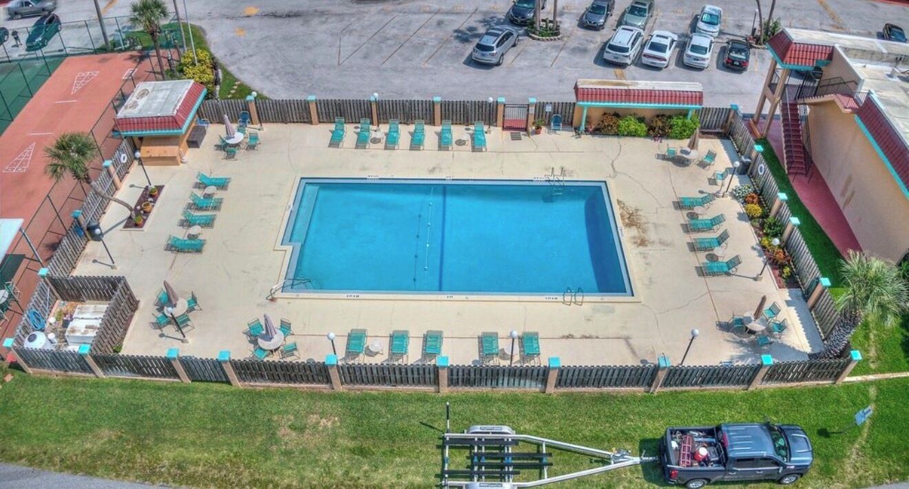 A rectangular swimming pool surrounded by lounge chairs and a fenced area.