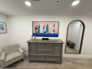 A room with a grey dresser, a framed painting of sailboats, a beige armchair, and a large mirror. - Cozy 2-bedroom condo in lovely St. Augustine across from the beach and Fun (St. Augustine)