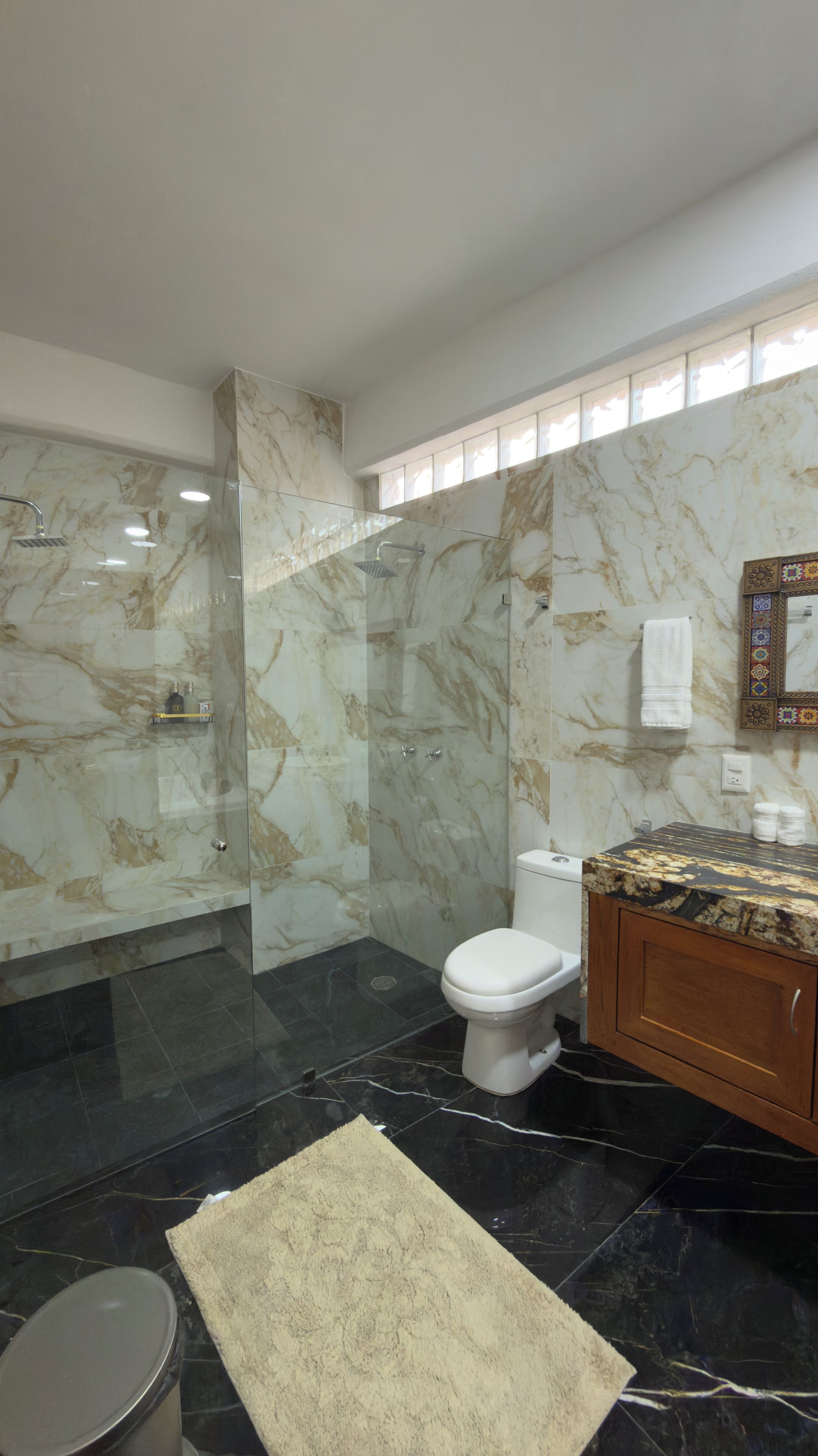 A modern bathroom with a glass-enclosed shower, a toilet, and a vanity with a marble countertop.