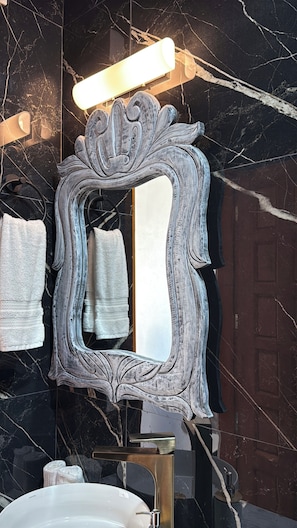 A bathroom with a marble wall, a white sink, a mirror with a decorative frame, and a towel rack with towels. - Villa SoL Boutique Hotel Puerto Vallarta (Puerto Vallarta)