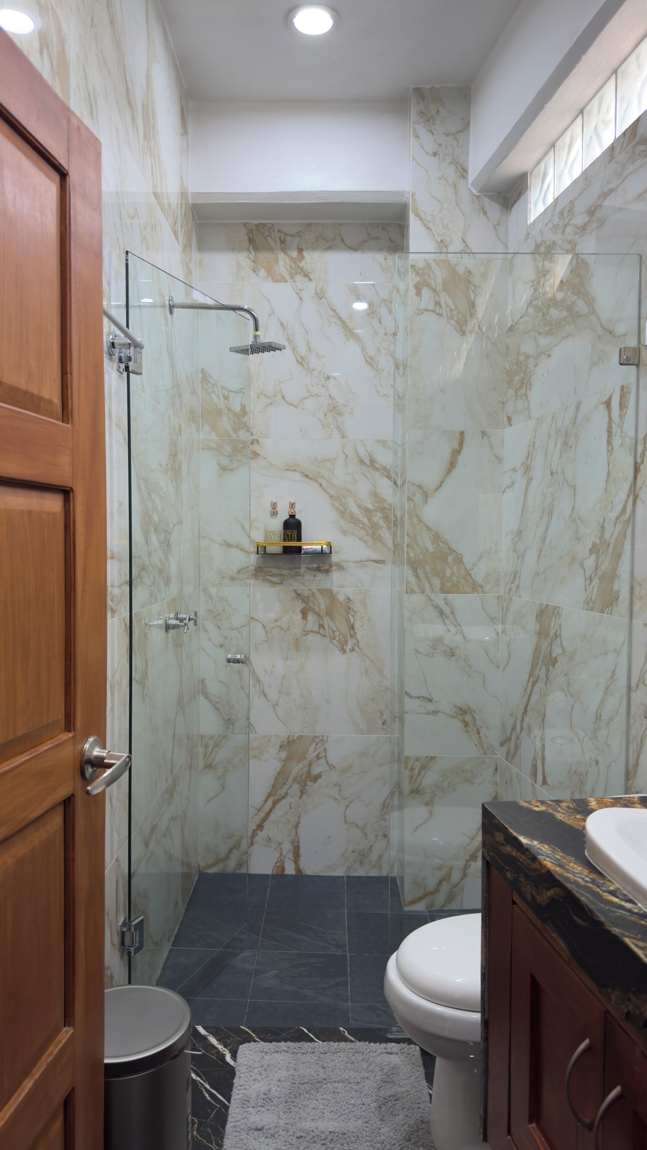A bathroom with a glass shower enclosure, a toilet, and a sink with a marble countertop.