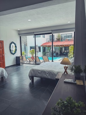 A modern hotel room with a large bed, a desk, a chair, and a view of a swimming pool and outdoor seating area. - Villa SoL Boutique Hotel Puerto Vallarta (Puerto Vallarta)