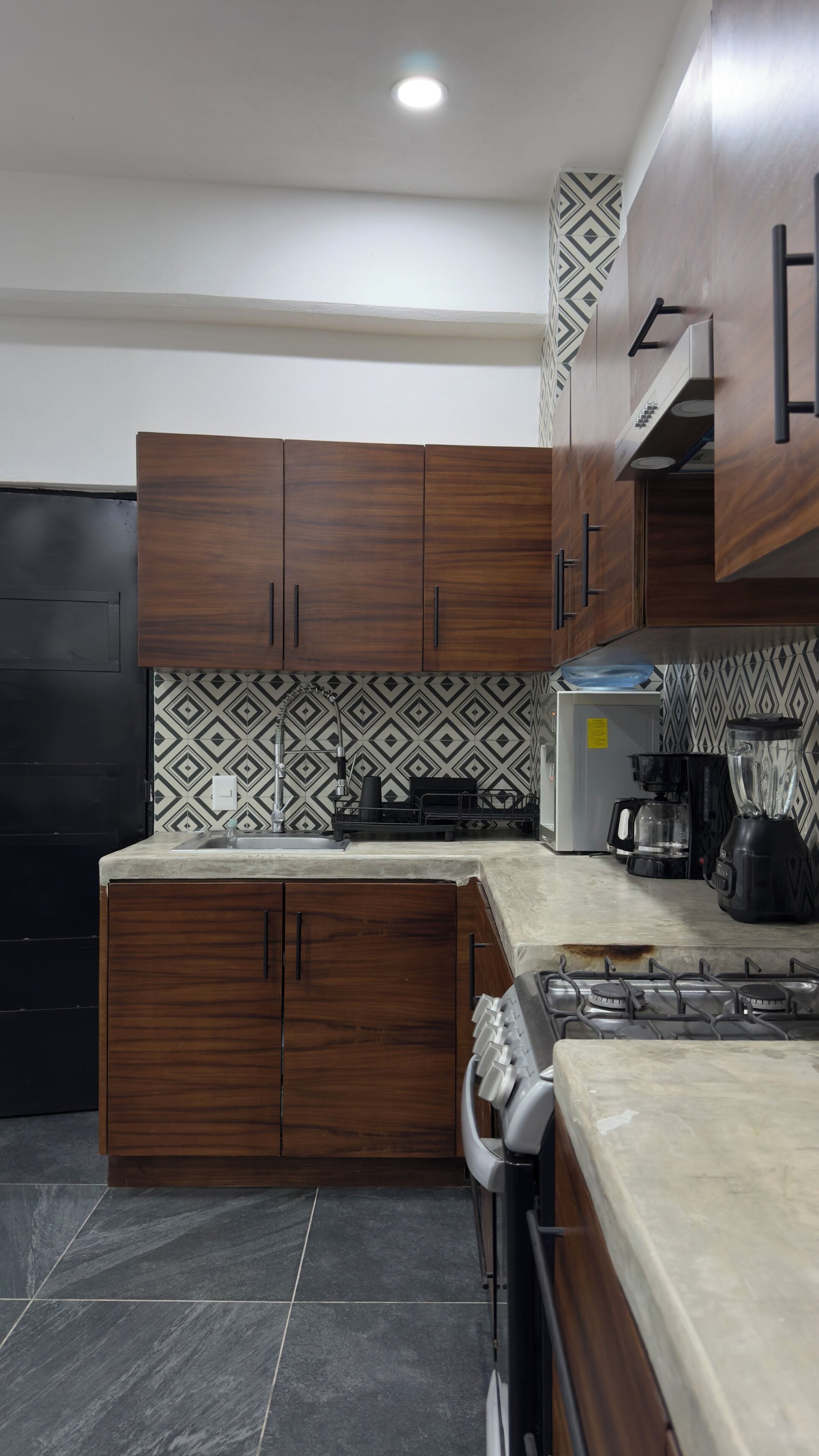 A kitchen with dark wooden cabinets, a patterned backsplash, a gas stove, a coffee maker, and a blender.