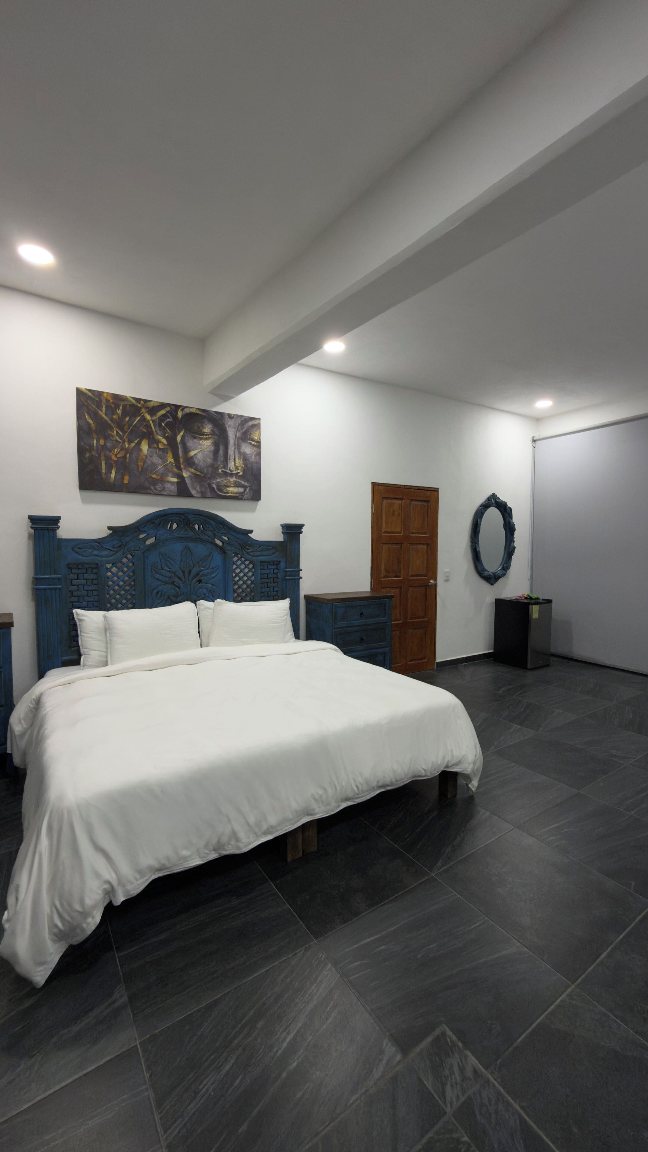 A bedroom with a large bed, a wooden door, a dresser, and a wall-mounted artwork.
