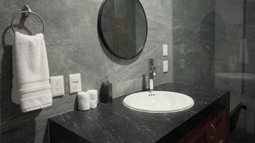 Un baño moderno con tocador de mármol negro, un espejo redondo y un lavabo blanco.