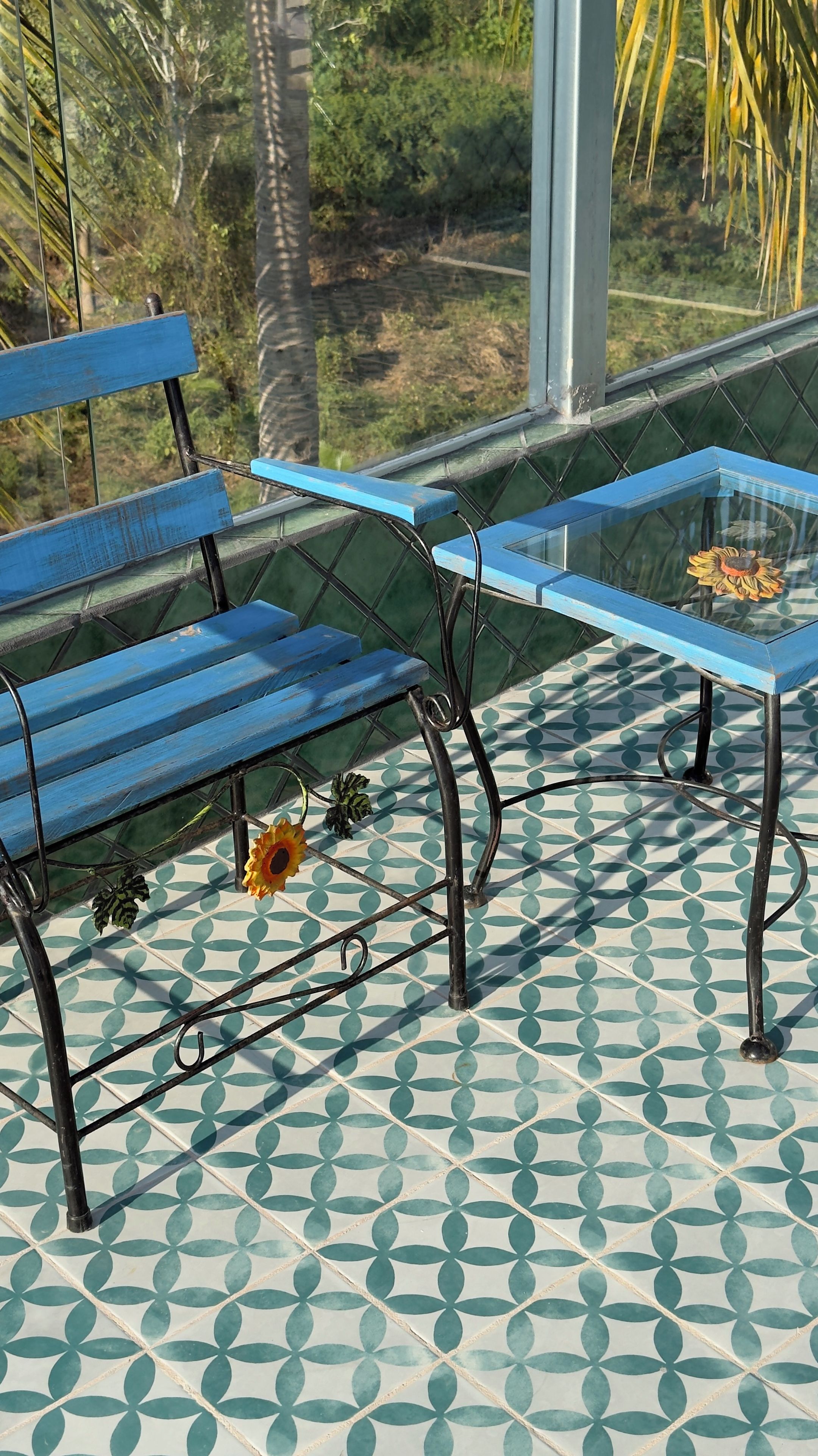 A blue bench and a glass table with a flower on a patterned floor.