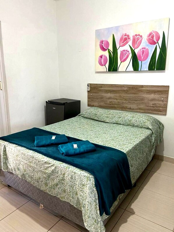 A bedroom with a bed, a nightstand, a painting of pink tulips, and a wooden headboard.
