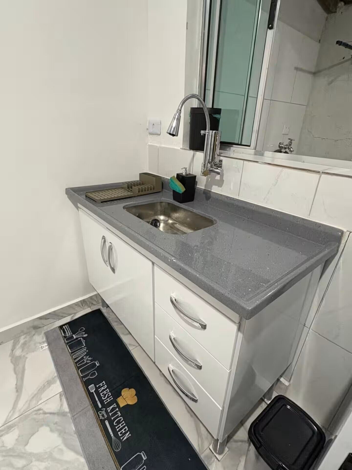 A kitchen with a stainless steel sink, a faucet, and a black trash bin.
