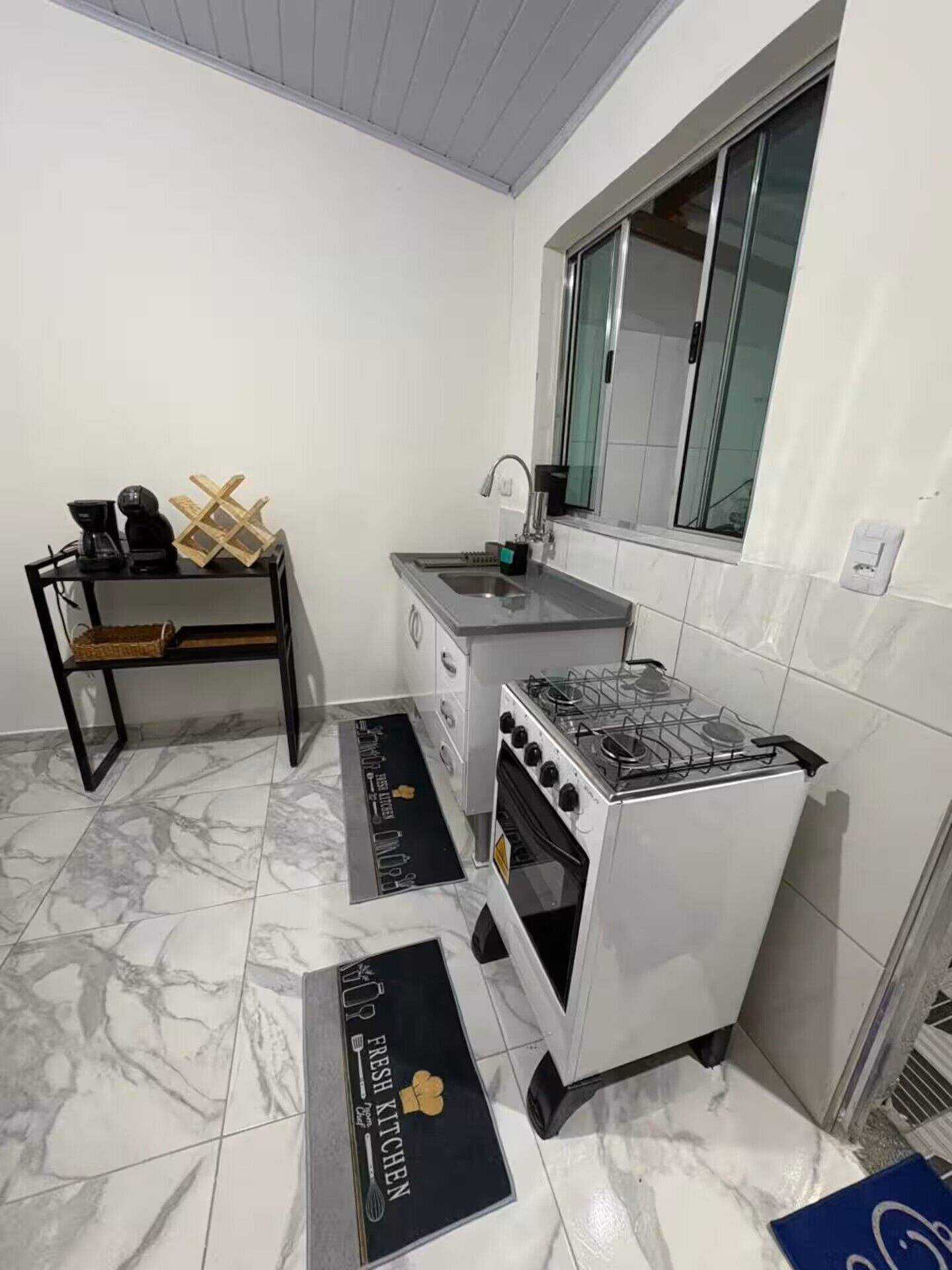 Cocina compacta con estufa a gas, un lavamanos y una ventana sobre la encimera.