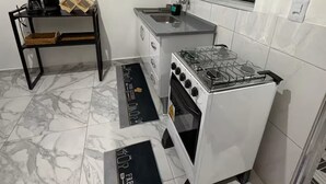 A compact kitchen with a gas stove, a sink, and a window above the countertop. - Studio 5 | Vila Granados (Embu das Artes)