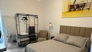 A bedroom with a bed, a chair, a wardrobe, and a painting on the wall. - Studio 5 | Vila Granados (Embu das Artes)
