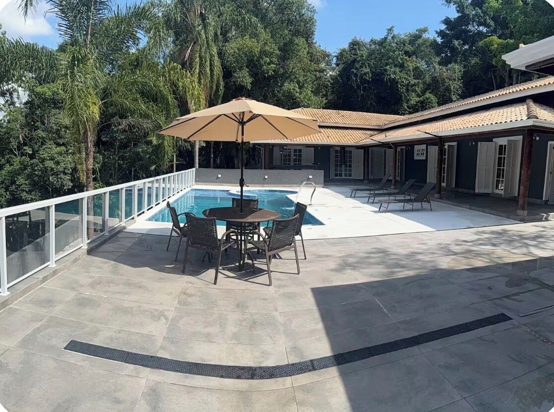 A pool area with a table and chairs, surrounded by a glass railing, and a covered seating area with umbrellas.