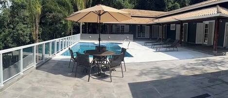 A pool area with a table and chairs, surrounded by a glass railing, and a covered seating area with umbrellas.