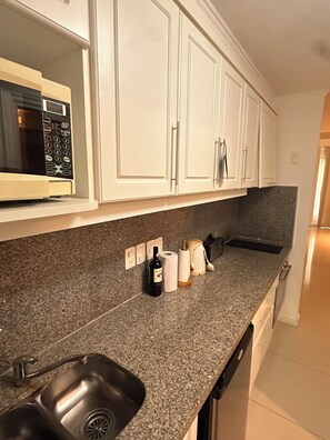 A kitchen with white cabinets, a granite countertop, a built-in microwave, a sink, and a coffee maker.