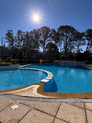 A swimming pool with a curved edge and a series of steps leading into the water, surrounded by trees and a clear sky.