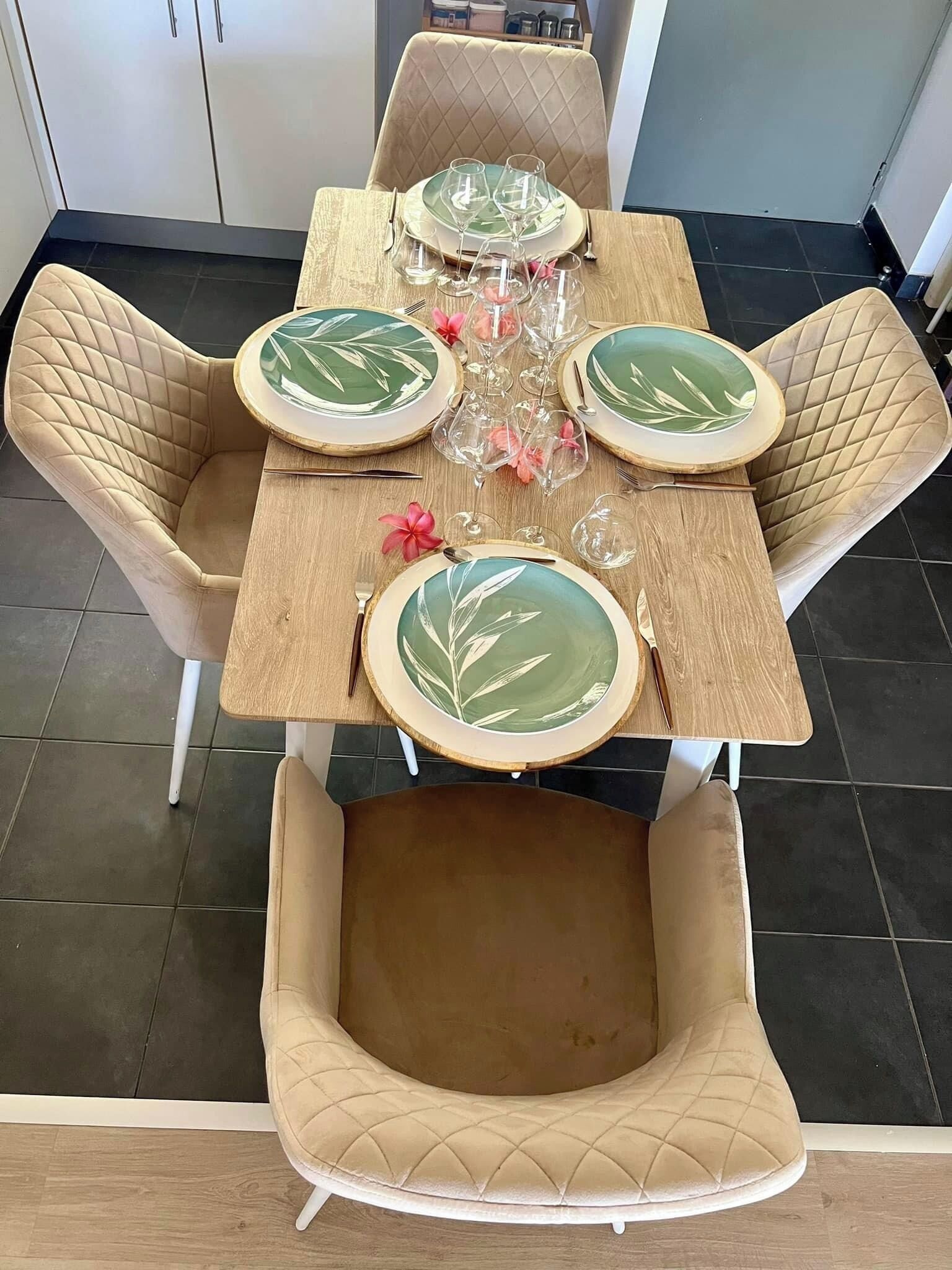 A dining table with four chairs, each with a cushioned seat and backrest. The table is set with plates, cutlery, and glasses.