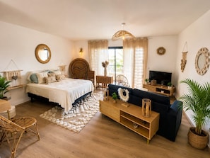 A well-lit room with a bed, a sofa, a TV, and a dining area.