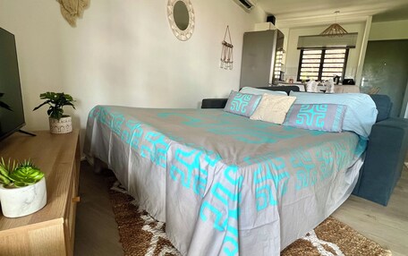 A bedroom with a bed, a television, a potted plant, and a decorative wall piece.