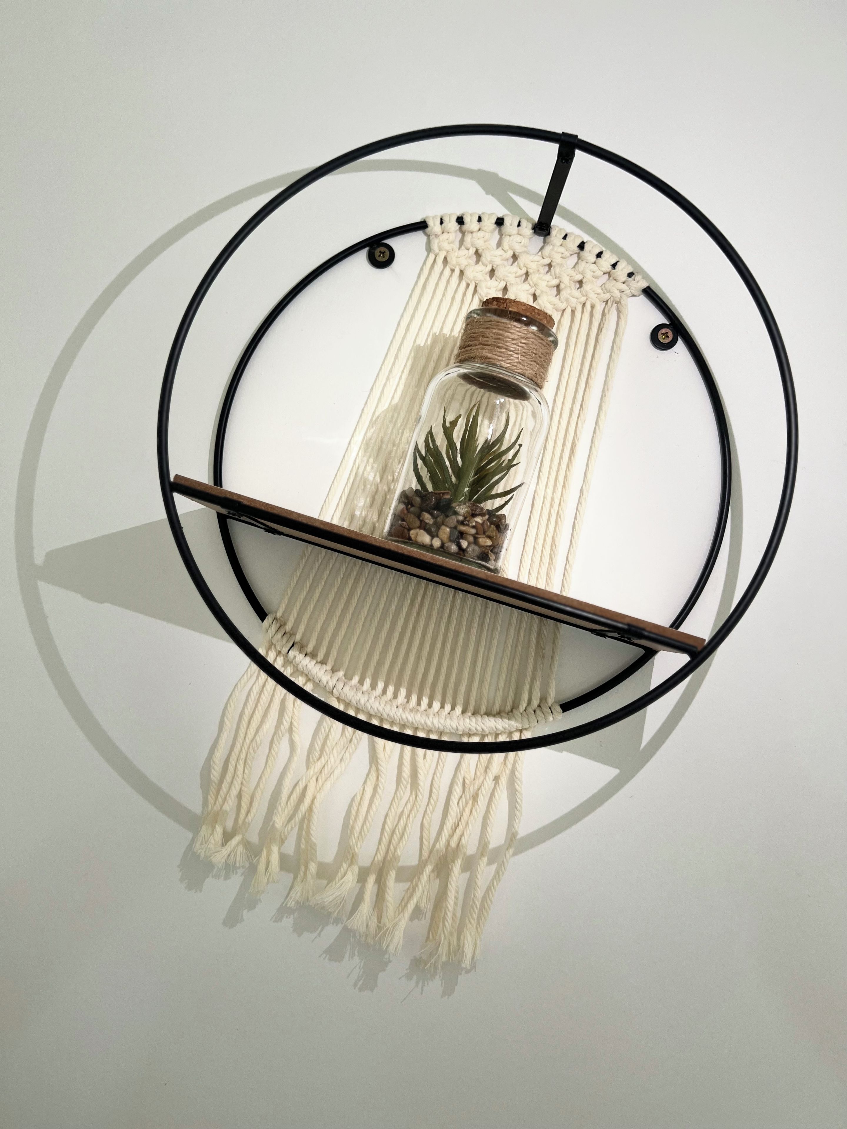 A wall-mounted macrame piece with a circular frame, a wooden shelf, and a pineapple decoration.