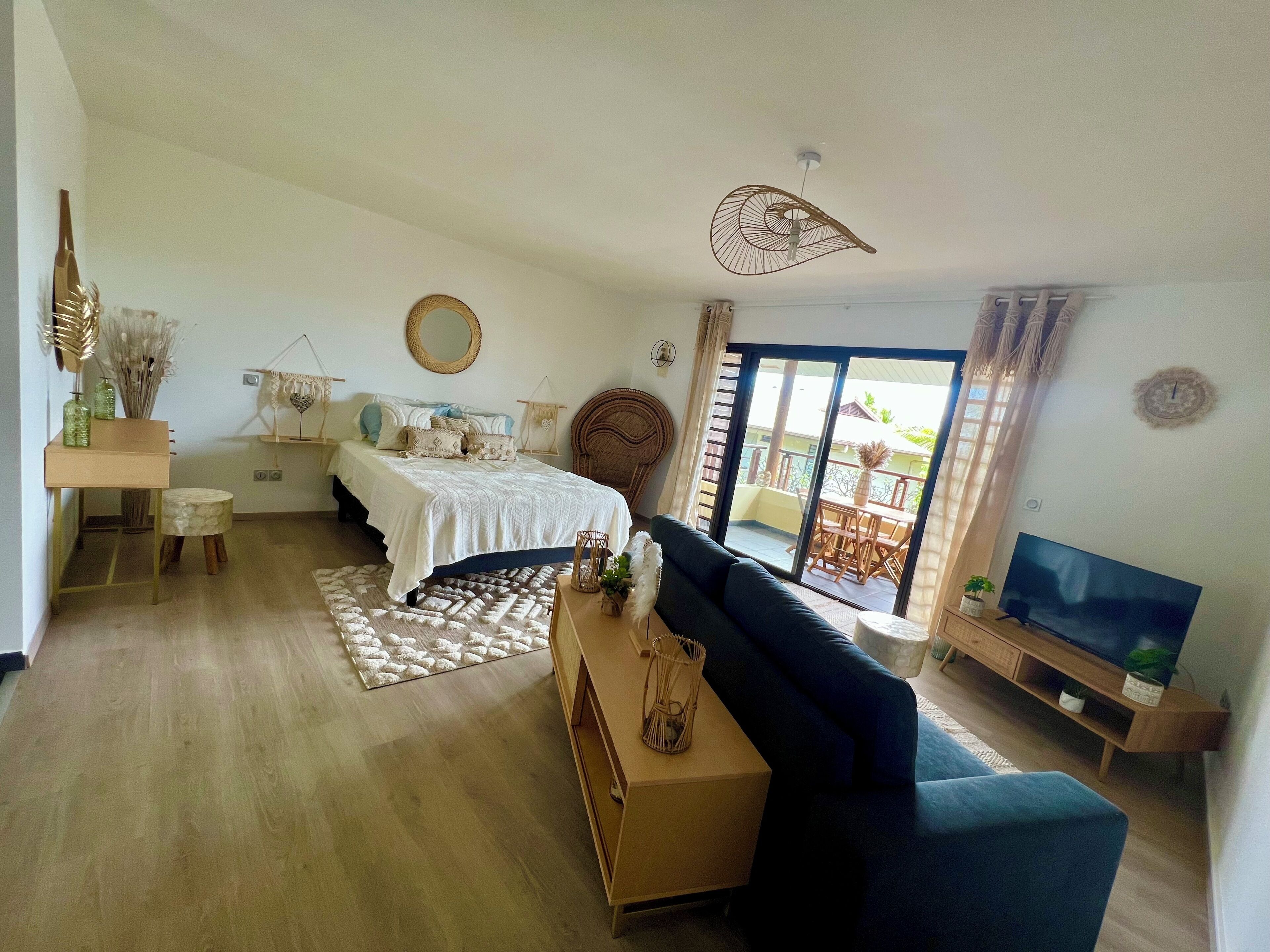 A modern living room with a bed, a sofa, a TV, and a balcony with outdoor furniture.