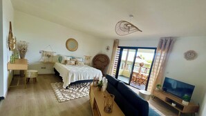 Una sala de estar moderna con una cama, un sofá, un televisor y un balcón con mobiliario exterior.