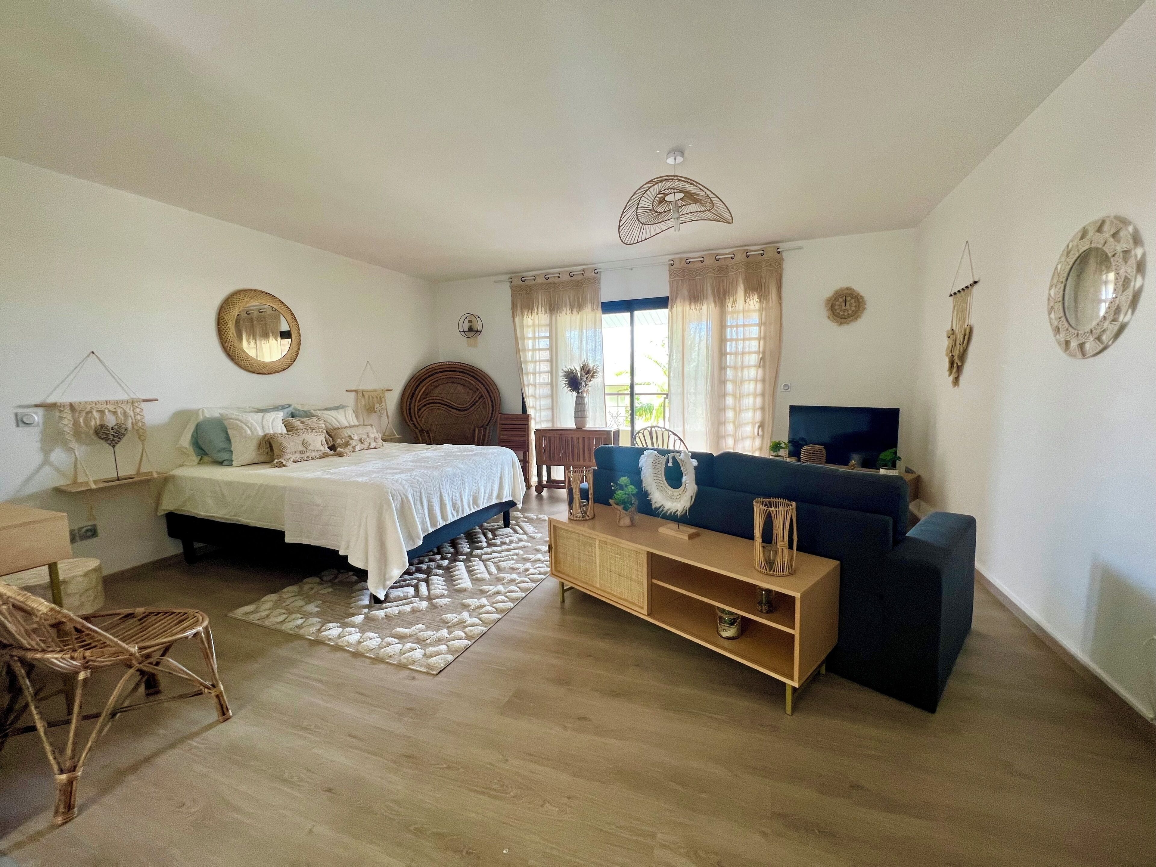 A well-lit room with a bed, a sofa, a TV, and a dining table.