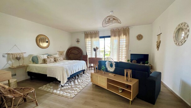 Una habitación luminosa con cama, sofá, televisor y mesa de comedor.