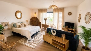 A well-lit room with a bed, a sofa, a TV, and a dining area.