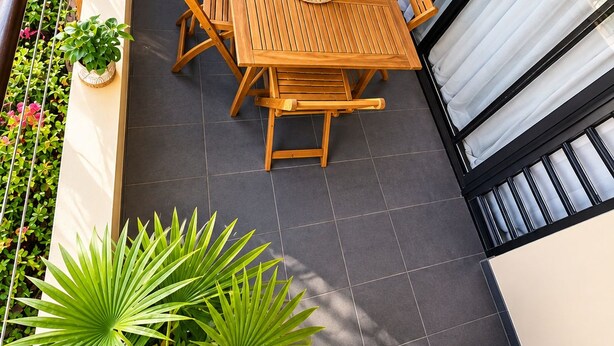 A balcony with a wooden table and chairs, surrounded by potted plants and a wicker chair.