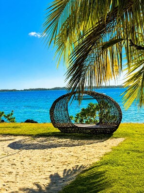 Escena de playa con una silla tejida y vista al océano.