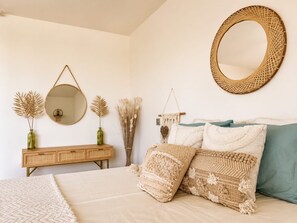 A bedroom with a bed, a dresser, a round mirror, and decorative items.