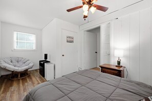 Une chambre à coucher comprenant un lit, une chaise, un bureau, un ventilateur de plafond et une fenêtre avec des stores.
