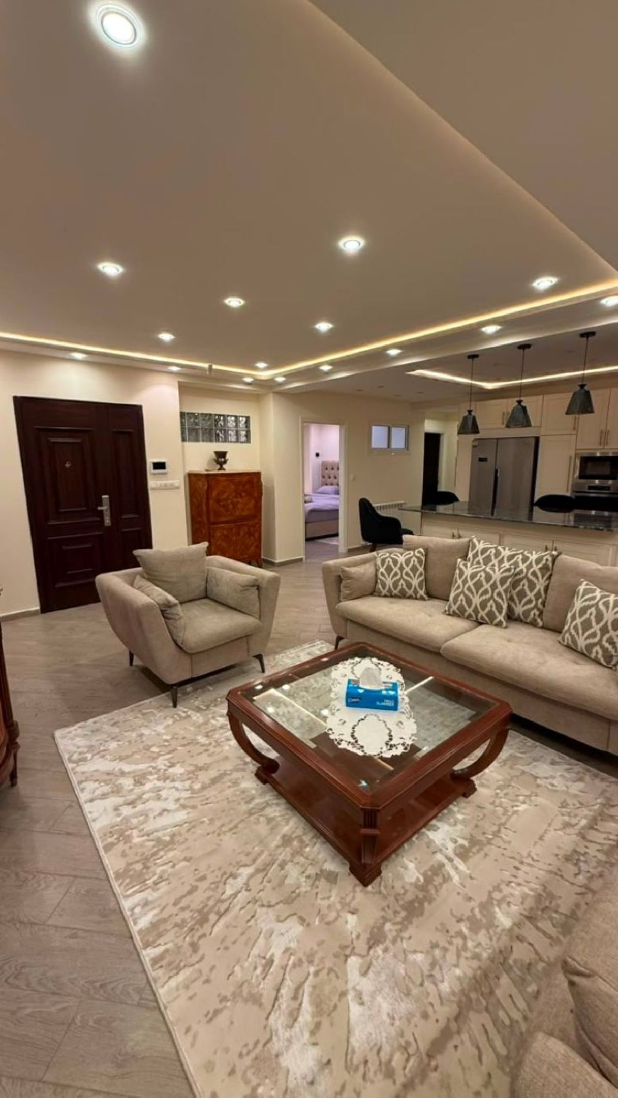 A modern living room with a sofa, armchairs, a coffee table, and a kitchen in the background.