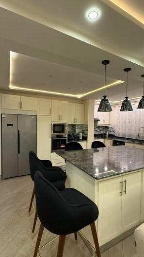 A modern kitchen with a central island, bar stools, stainless steel appliances, and pendant lighting. - Élégance à Kouba – 3 chambres, suite & garage. (Kouba)