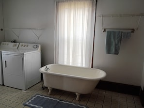 Un baño con una bañera blanca, una lavadora y un tendedero.