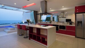 A modern kitchen with a central island, red cabinetry, and a view of the sea. - Central Villa With Mountain & sea View (Koh Samui)