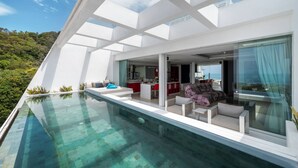 A modern house with a glass infinity pool, a dining area, and a living room with a view of the ocean. - Central Villa With Mountain & sea View (Koh Samui)