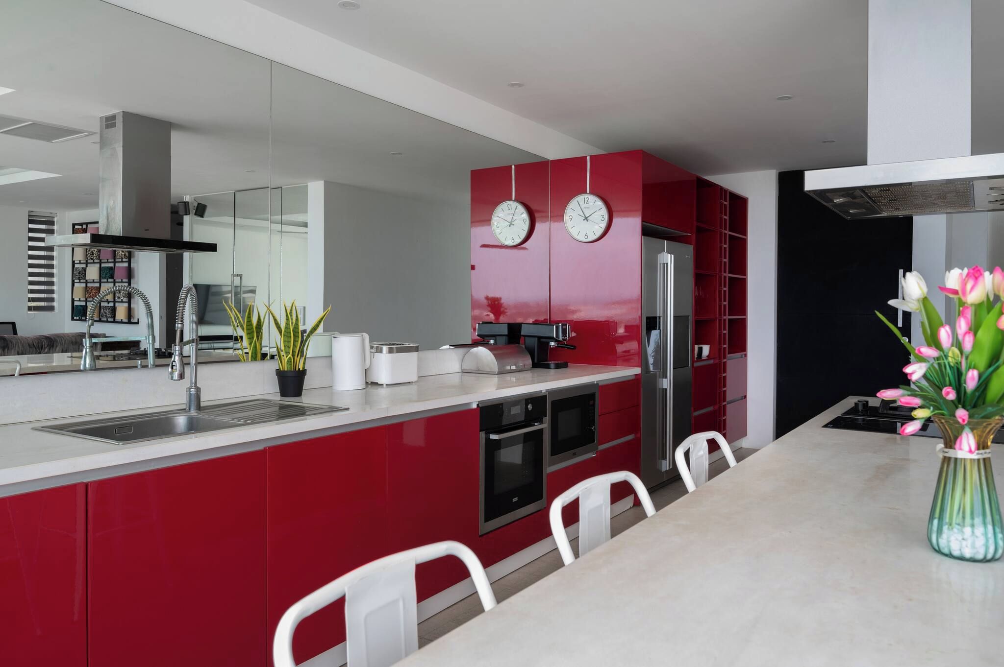 A modern kitchen with red cabinetry, stainless steel appliances, and a dining area with white chairs.