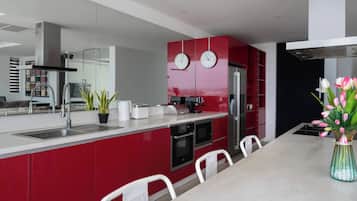 A modern kitchen with red cabinetry, stainless steel appliances, and a dining area with white chairs.